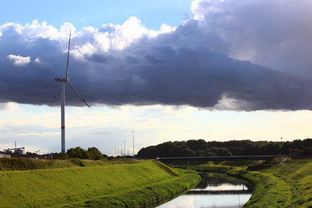 A wind turbine in a peaceful landscape with green grass, blue skye and a riverの写真素材