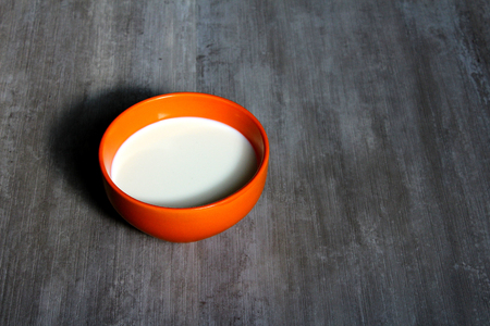 An orange bowl with milk on a grey backgroundの写真素材