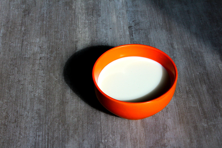 An orange bowl with milk on a grey backgroundの写真素材