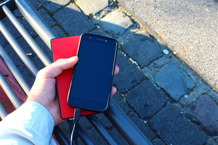 A black smartphone and a red powerbank in a male hand on the benchの写真素材