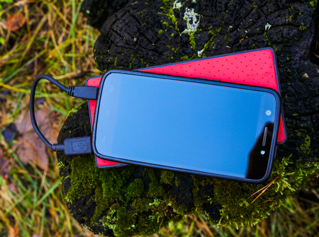 Black smartphone and  red powerbank on tree stumpの写真素材