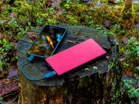 Black smartphone and  red powerbank on tree stumpの写真素材