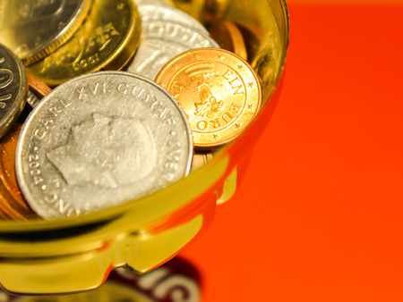 Golden copper and silver coins in a cup with light orange background