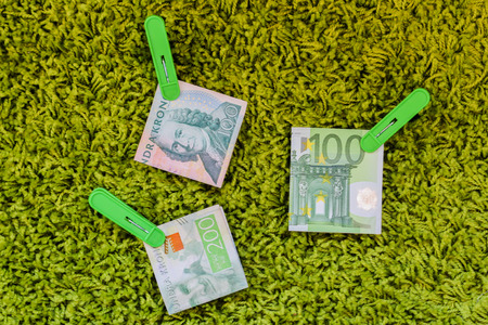 Three green banknotes 100 euro 100 swedish crownes and 200 swedish crownes in green clothes pegs at a green backgroundの写真素材