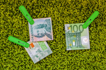 Three green banknotes 100 euro 100 swedish crownes and 200 swedish crownes in green clothes pegs at a green backgroundの写真素材
