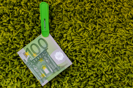 Green banknote 100 euro in a green clothes peg at a green backgroundの写真素材