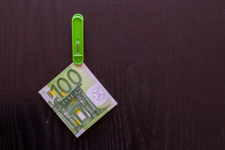 Green banknote 100 euro in a green clothes peg at a black wooden backgroundの写真素材