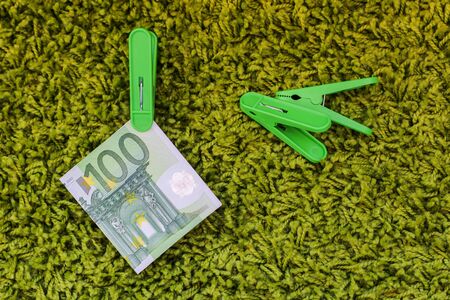 Green banknote 100 euro in a green clothes peg at a green backgroundの写真素材