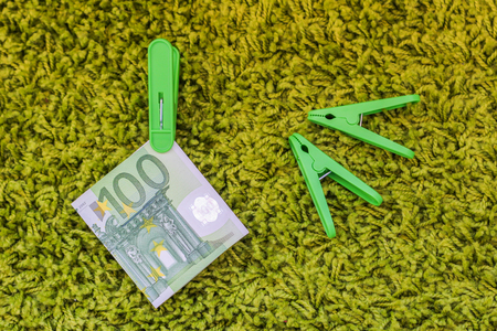 Green banknote 100 euro in a green clothes peg at a green backgroundの写真素材