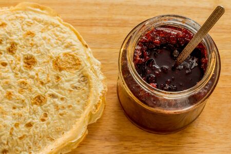 Pancake with silver spoon and red cranberry jam on a wooden board
