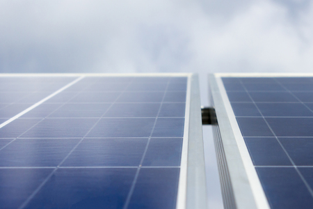 Blue solar panels against background of sky with clouds, view from below