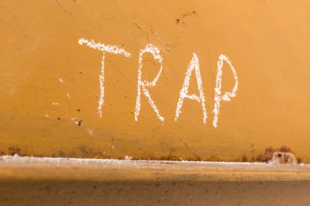 Word trap handwriting with white chalk on old orange metal background with a fly trapped in spider webの写真素材