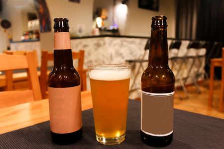 Two beer bottles and full glass of light orange juicy tasty beer in a cozy craft beer bar