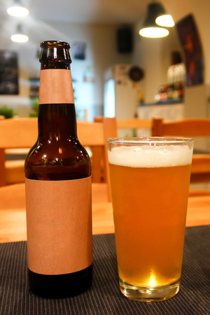 One beer bottle and full glass of light orange juicy tasty beer in a cozy craft beer barの写真素材
