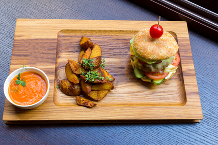 Delicious burger with meat, vegetables, potatoes and orange sauce on a wooden platter backgroundの写真素材