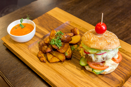 Delicious burger with meat, vegetables, potatoes and orange sauce on a wooden platter backgroundの写真素材