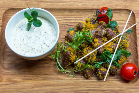 Pieces of beef or pork meat and white sauce with vegetables on brown wooden platter backgroundの写真素材