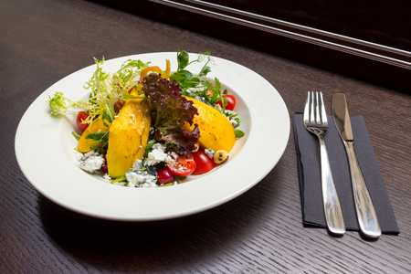 Dessert salad with mango and goat cheese, and fork and knife on black wooden table backgroundの写真素材