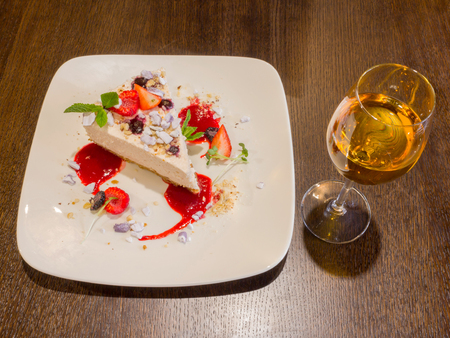 Cheescake with strawberies and a glass of orange wine on wooden table backgroundの写真素材