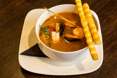 Delicious seafood soup with shrimps, prawns, oysters, mussels and jelly in a white soup plate on brown table backgroundの写真素材