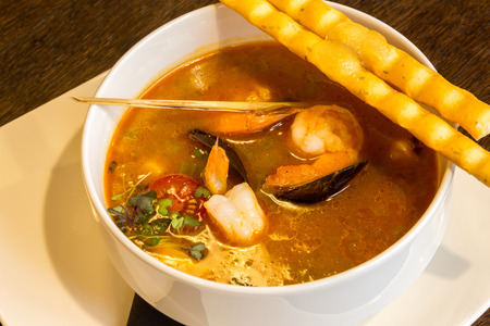 Delicious seafood soup with shrimps, prawns, oysters, mussels and jelly in a white soup plate on brown table backgroundの写真素材