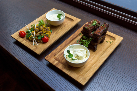 Chicken hear meat snack and roasted garlic bread snack with white sauces on wooden platters on black table background angle viewの写真素材