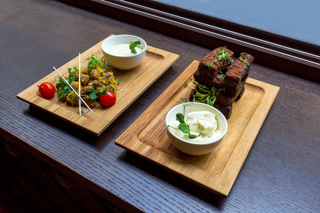Chicken hear meat snack and roasted garlic bread snack with white sauces on wooden platters on black table background top viewの写真素材