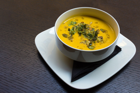 Root vegetable yellow cream soup on black wooden table backgroundの写真素材