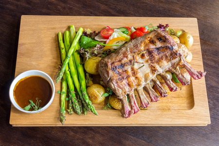 Delicious lamb meat crown roast with vegetable salad and brown sauce on wooden platter on brown wooden tableの写真素材