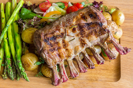 Delicious lamb meat crown roast with vegetable salad and brown sauce on wooden platter on brown wooden tableの写真素材