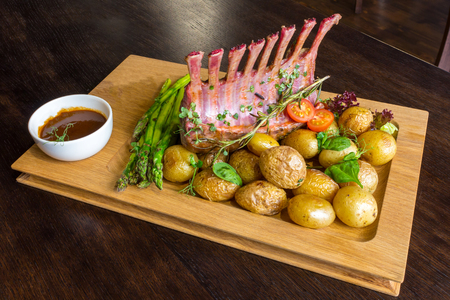 Delicious lamb meat crown roast with vegetable salad and brown sauce on wooden platter on brown wooden tableの写真素材