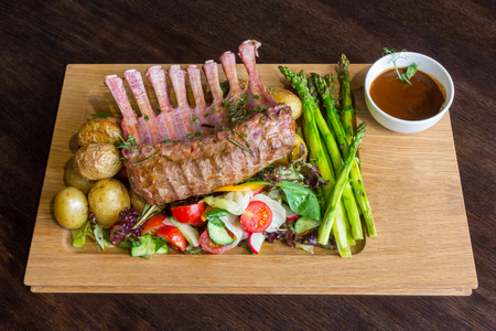 Delicious lamb meat crown roast with vegetable salad and brown sauce on wooden platter on brown wooden tableの写真素材