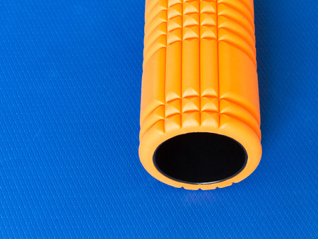 Orange fitness foam roller on blue scale texture background top view with copy spaceの写真素材