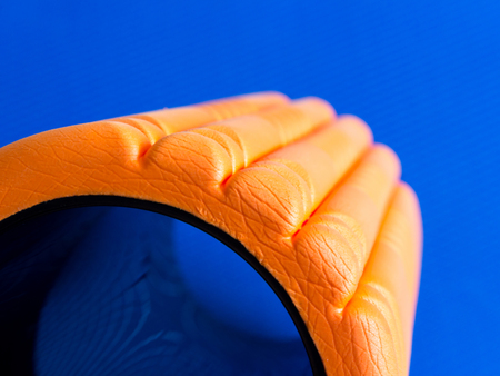 Orange fitness foam roller on blue background with beautiful reflection closeup with copy spaceの写真素材