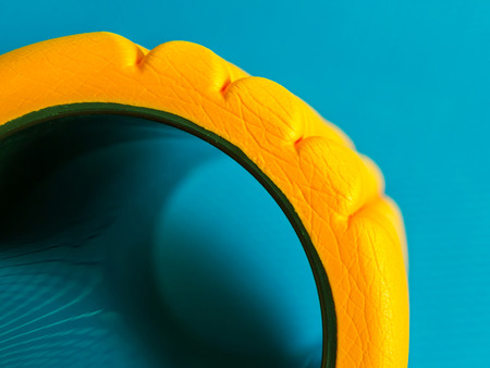 Yellow fitness foam roller on blue background with beautiful reflection closeup with copy spaceの写真素材