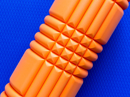 Orange fitness foam roller on blue scale texture background with diagonal orientation top viewの写真素材