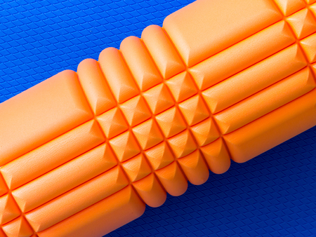 Orange fitness foam roller on blue scale texture background top viewの写真素材