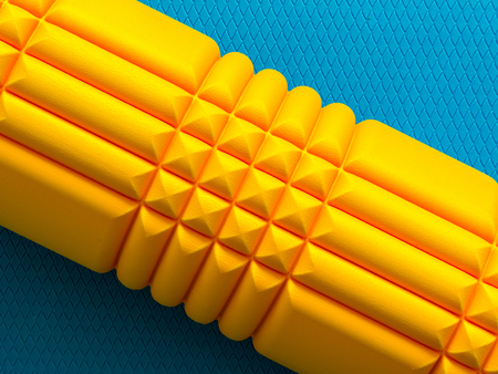Yellow fitness foam roller on blue scale texture background top viewの写真素材