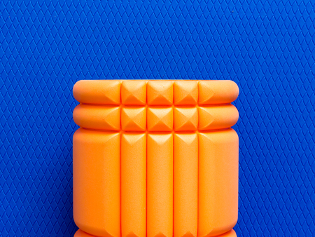 Orange fitness foam roller on blue scale texture background top viewの写真素材