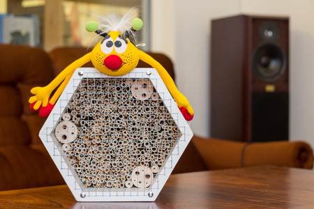 White wooden insect hotel in a light room on a brown table with a toy honey bee on topの写真素材