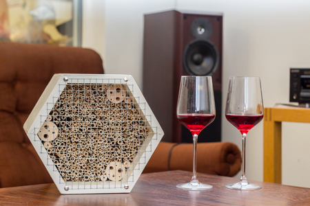 White wooden insect hotel in a light room on a table with two red wine glassesの写真素材