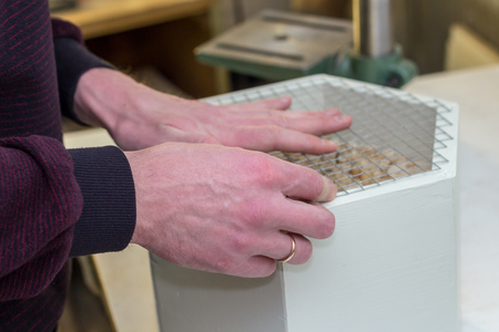 Hands of a man making a wooden white insect hotel, filling the insect house with reed and closing with a netの写真素材