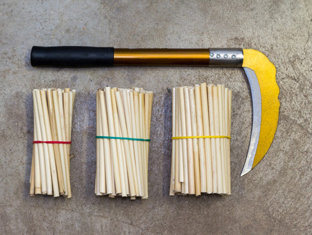 Yellow sickle with black handle and reed harvest bundle on cracked concrete floorの写真素材