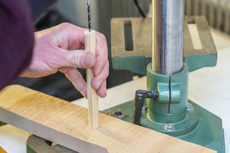 Worker hand holding a wooden detail and processing it with a boring machine on a work bench in a workshopの写真素材