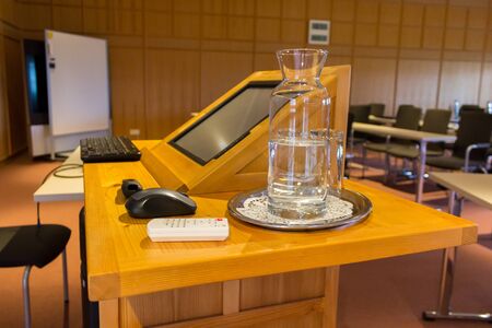 Wooden trubune in a conference or lecture hall with a water pitcher and a computerの写真素材