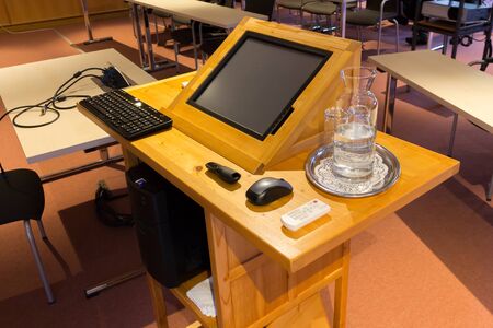 Wooden trubune in a conference or lecture hall with a water pitcher and a computer screenの写真素材