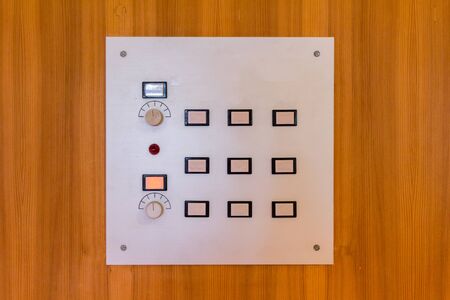 White control panel on a wooden wall with white, blue and red buttons and regulatorsの写真素材