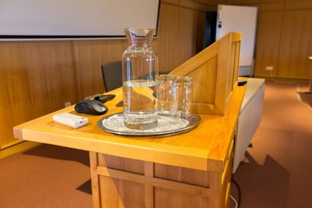 Wooden trubune in a conference or lecture hall with a water pitcher and a screenの写真素材
