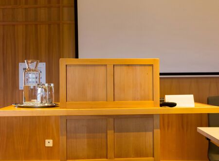 Wooden trubune in a conference or lecture hall with a water pitcher and a projector screenの写真素材