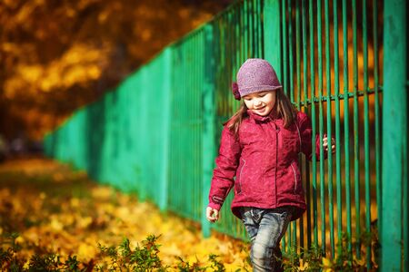 child near the green fence on the background of fallの写真素材